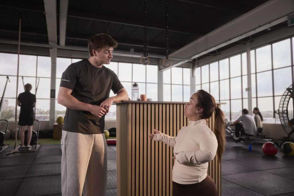 man en een vrouw staan met elkaar in gesprek in een sportschool bij de balie